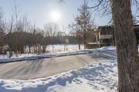 a winter scene with sun shining over the trees and road leading to a parking area