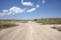 a dirt road next to a grassy field under clouds in the sky near a sign with no stopping