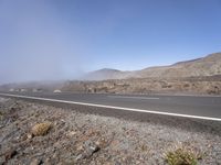 a road near the mountain side in the foggy sun day, and on the opposite bank are hills