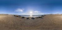 a fisheye image of a beach scene taken from sand area in front of water and rocks