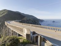 a highway with a sea view below a stone bridge near the ocean and some rocks