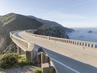 a highway with a sea view below a stone bridge near the ocean and some rocks