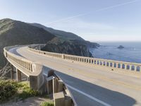 a highway with a sea view below a stone bridge near the ocean and some rocks