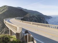 a highway with a sea view below a stone bridge near the ocean and some rocks