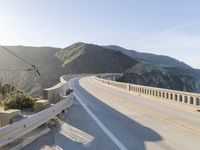 a highway with a sea view below a stone bridge near the ocean and some rocks