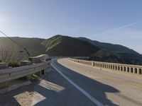 a highway with a sea view below a stone bridge near the ocean and some rocks