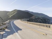 a highway with a sea view below a stone bridge near the ocean and some rocks