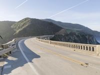 a highway with a sea view below a stone bridge near the ocean and some rocks