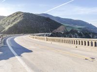 a highway with a sea view below a stone bridge near the ocean and some rocks