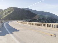 a highway with a sea view below a stone bridge near the ocean and some rocks