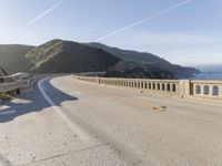 a highway with a sea view below a stone bridge near the ocean and some rocks