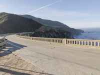 a highway with a sea view below a stone bridge near the ocean and some rocks