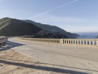 a highway with a sea view below a stone bridge near the ocean and some rocks