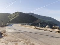 a highway with a sea view below a stone bridge near the ocean and some rocks