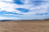 a large area of dirt with a blue sky and mountain in the background with clouds