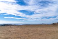 a large area of dirt with a blue sky and mountain in the background with clouds