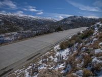 a very steep slope down to the highway and mountains in winter time with snow on it