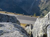 a man is riding a motorcycle down the hill side of a mountain side road and some rocks