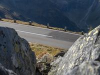 a man is riding a motorcycle down the hill side of a mountain side road and some rocks