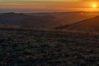 there is a sunset in the horizon on a field with grassy land below the mountains