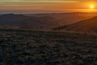 there is a sunset in the horizon on a field with grassy land below the mountains