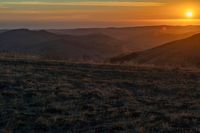 there is a sunset in the horizon on a field with grassy land below the mountains