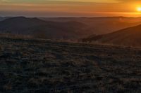 there is a sunset in the horizon on a field with grassy land below the mountains