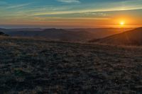 there is a sunset in the horizon on a field with grassy land below the mountains