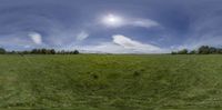 a green grassy field with mountains in the background and clouds over the grass is in a circular panorama format