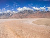 there is a desert plain with hills in the background and the sky is blue and there are clouds above