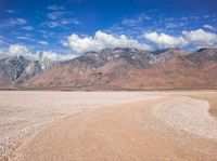 a dirt road passing through a barren valley of barren land with mountains and clouds in the distance