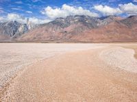 a dirt road passing through a barren valley of barren land with mountains and clouds in the distance