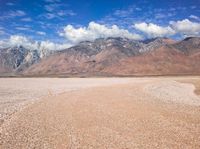 a dirt road passing through a barren valley of barren land with mountains and clouds in the distance