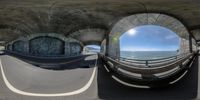 a fisheye view of an empty road near the ocean with a bridge over it