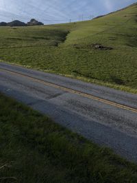 a grassy hill with electric wire fence in the foreground and distant country side with a road in the distance