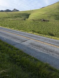 a grassy hill with electric wire fence in the foreground and distant country side with a road in the distance