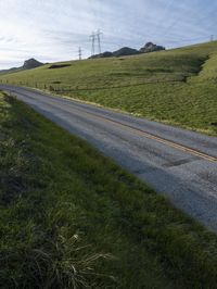 a grassy hill with electric wire fence in the foreground and distant country side with a road in the distance