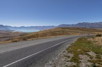 a lone bike rider riding down a hilly road surrounded by hills and lake water in the background