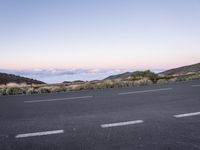 an empty winding road on a mountain with the sun set above the mountains in the background