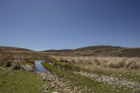 a stream runs through a barren area between two mountains on a clear day with some grass