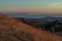 there is a sunset in the horizon on a field with grassy land below the mountains