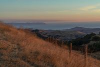 there is a sunset in the horizon on a field with grassy land below the mountains