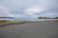 empty parking lot next to an ocean with a view of the coast and mountains on the shore