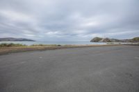 empty parking lot next to an ocean with a view of the coast and mountains on the shore