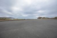 empty parking lot next to an ocean with a view of the coast and mountains on the shore