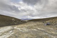 a dirt road with lots of rocks and gravel on it under a cloudy sky with many small clouds