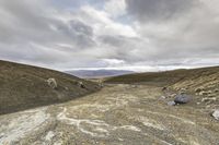 a dirt road with lots of rocks and gravel on it under a cloudy sky with many small clouds