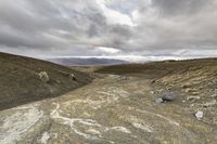 a dirt road with lots of rocks and gravel on it under a cloudy sky with many small clouds