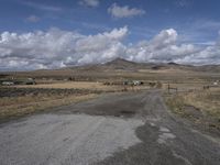 an empty dirt road and small fence in a grassy landscape in the distance, is a mountain range