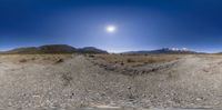 panorama of a desert with dirt, rocks and a very bright sun in the sky